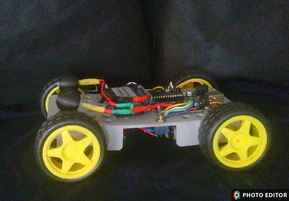Bluetooth-controlled car with four yellow wheels, a gray chassis, mounted electronics, battery, and wiring.
